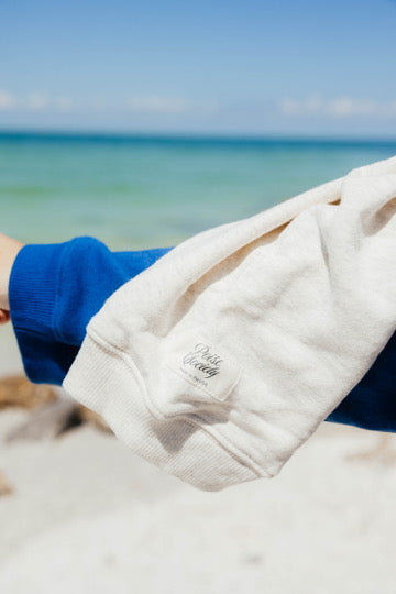 usa made, elevated basics, matching set, terry cloth crew Person wearing a white jacket with a logo on a beach